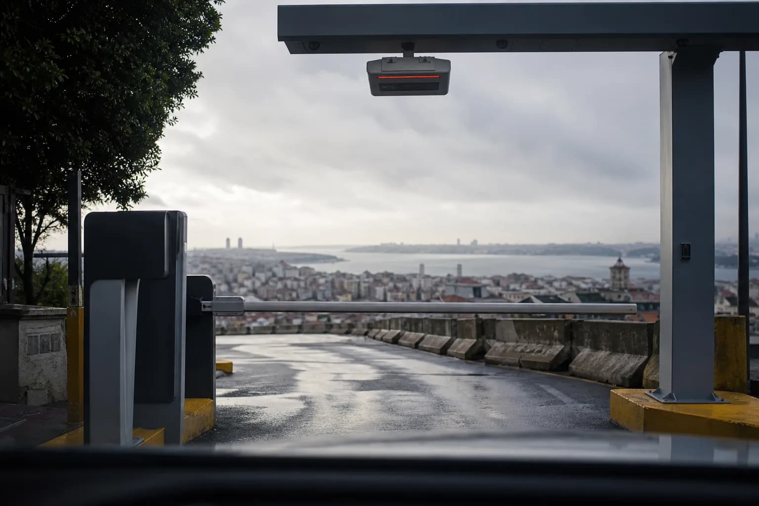 Sürücü açısından bir otoparkın açık bariyeri, şerit üstündeki plaka okuyucu ve arkada İstanbul Boğazı.
